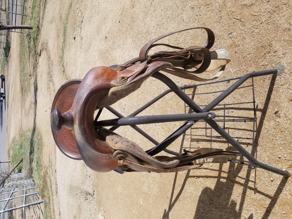 A saddle on the ground with a metal stand.