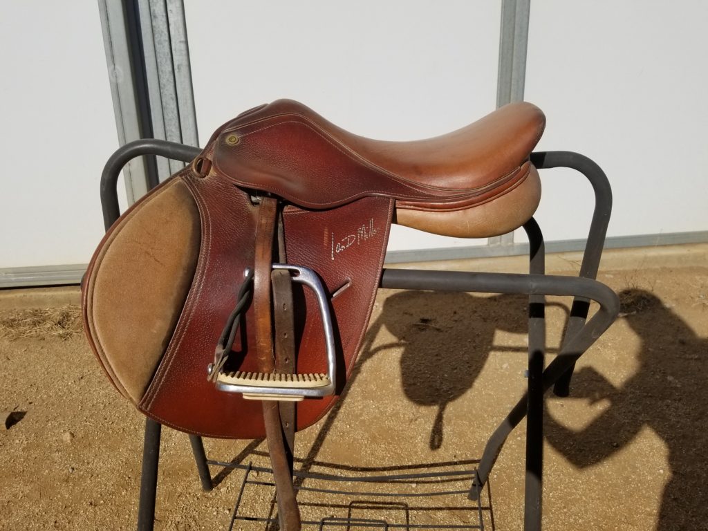 A saddle on top of a rack in front of a wall.