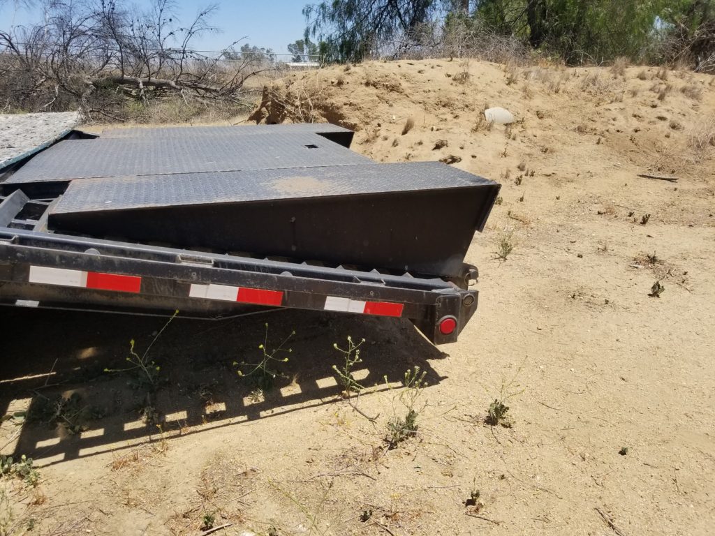 A black trailer is parked in the dirt.